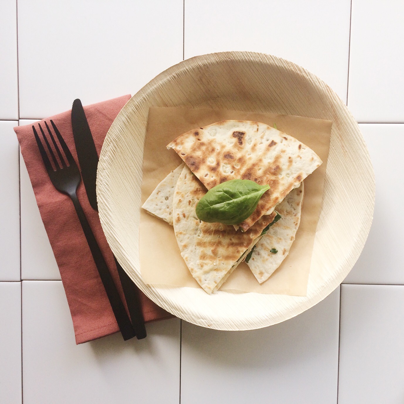 Flatlay van houten bord met 4 stukjes quessedilla en rode servet met zwart bestek