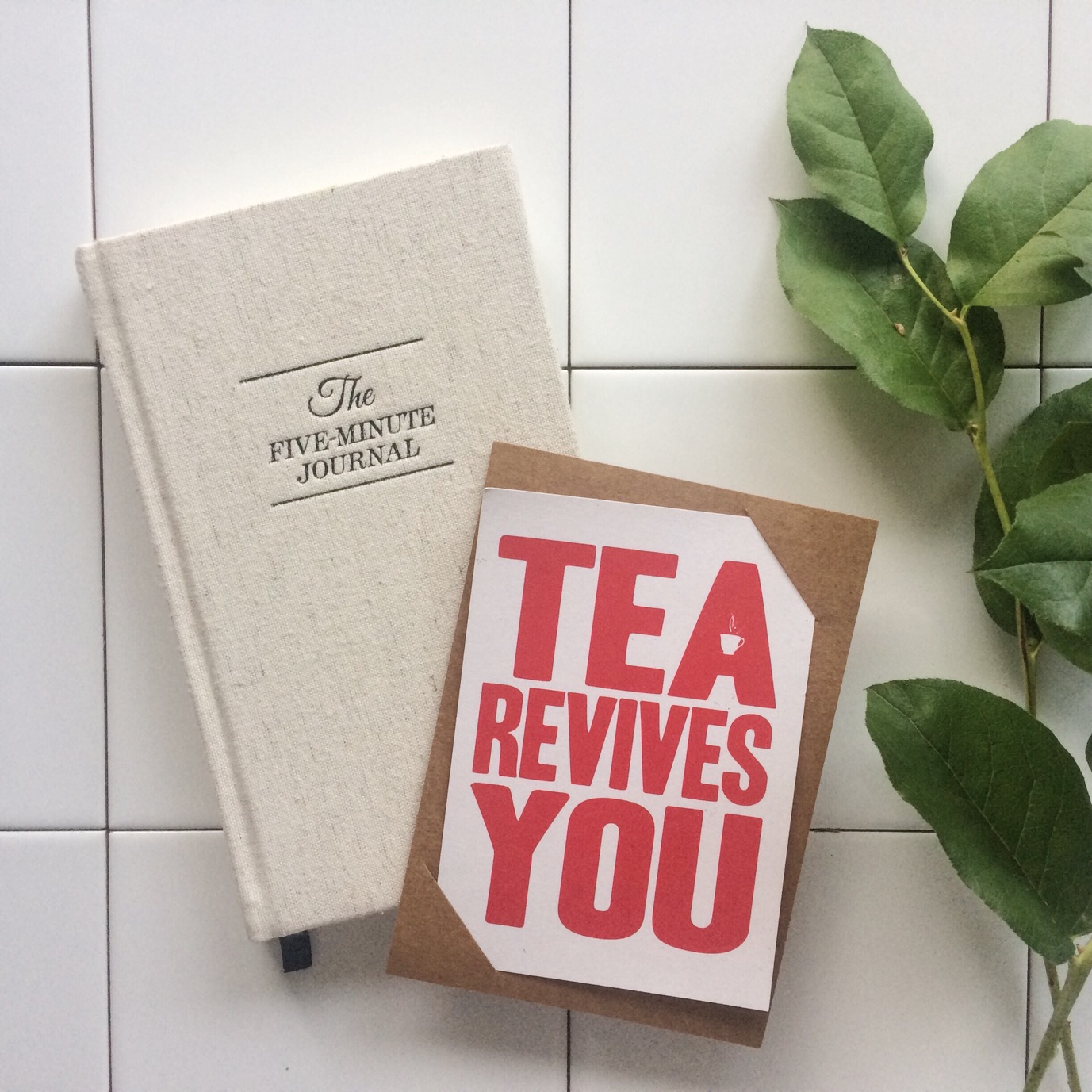 Flatlay met 5 minute journal, kaar met quote 'tea revives you' en groen takje