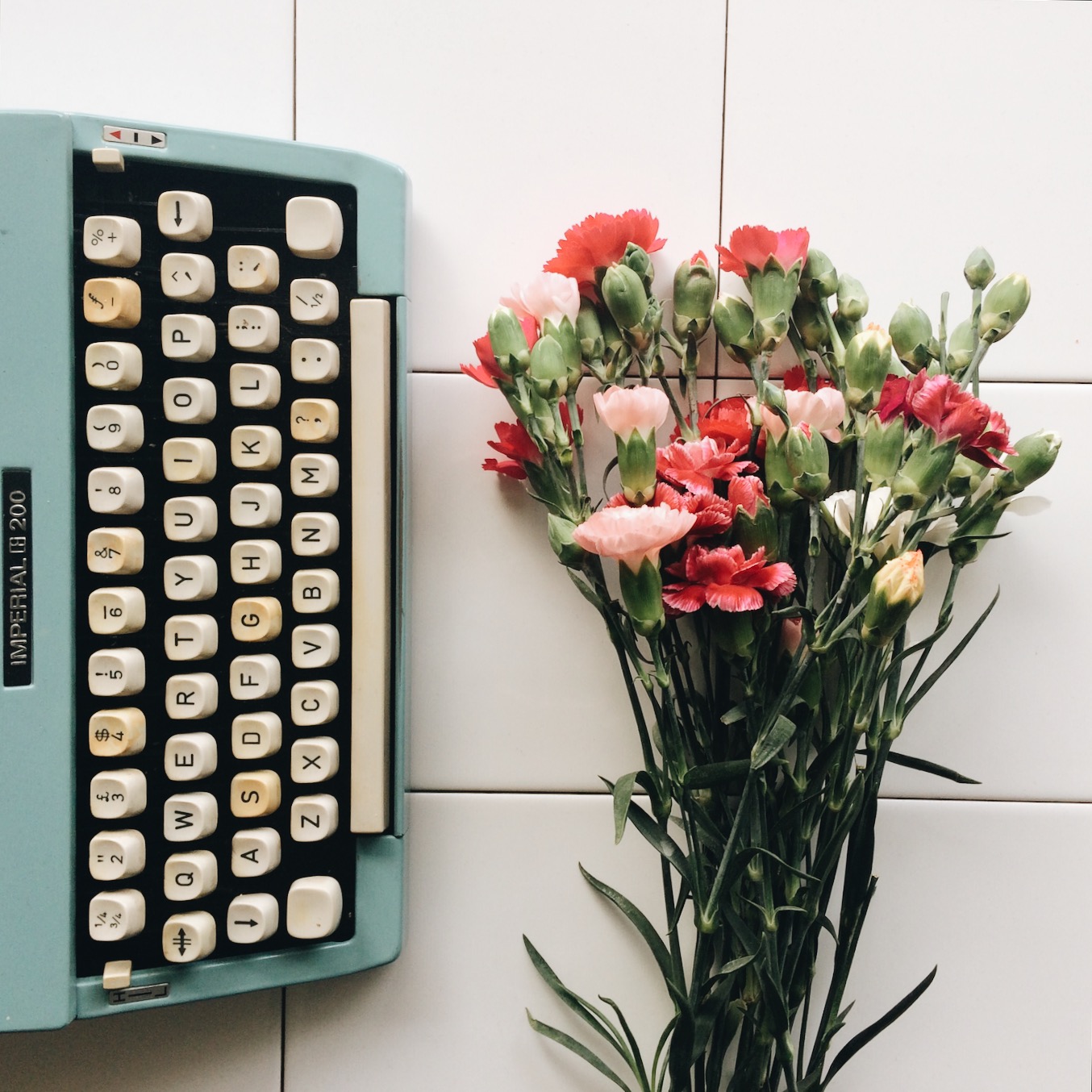 Flatlay van retro pastel blauwe typemachine met daarnaast een bos felgekleurde anjers